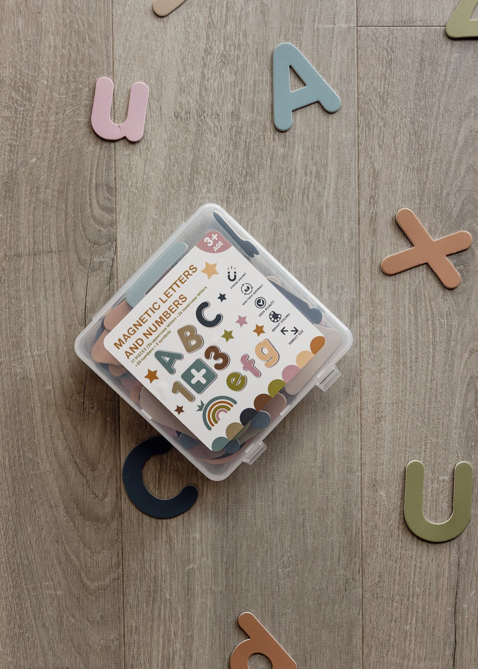 ABC & 123 magnetic letters and numbers in a clear storage box, surrounded by colourful letters on a wooden floor