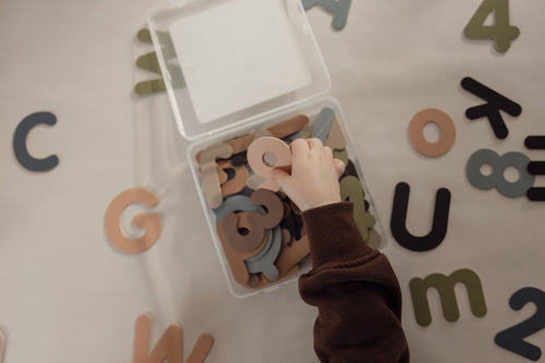 Child's hand reaching into a clear box of magnetic letters and numbers in soft, muted colours