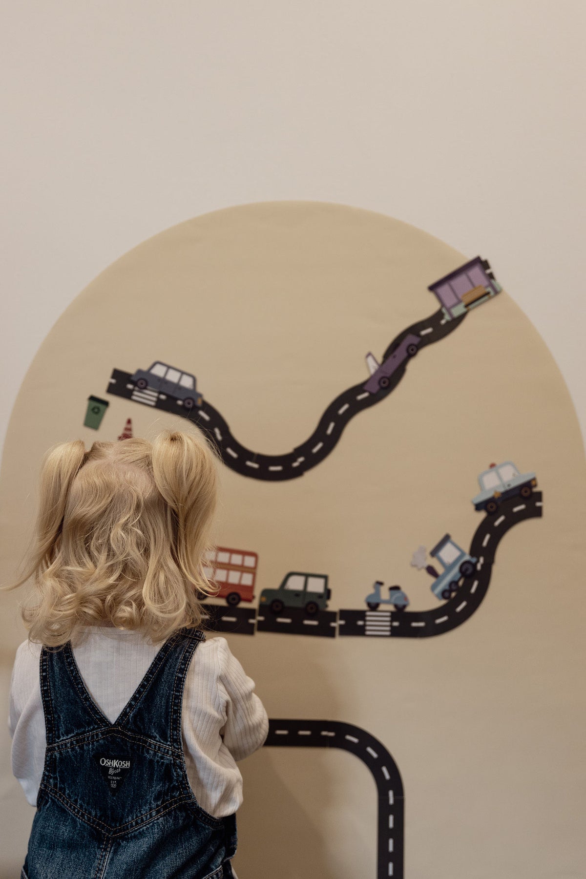 Toddler in denim overalls building a road scene with car magnets on the Arlo Beige Wonder Arch