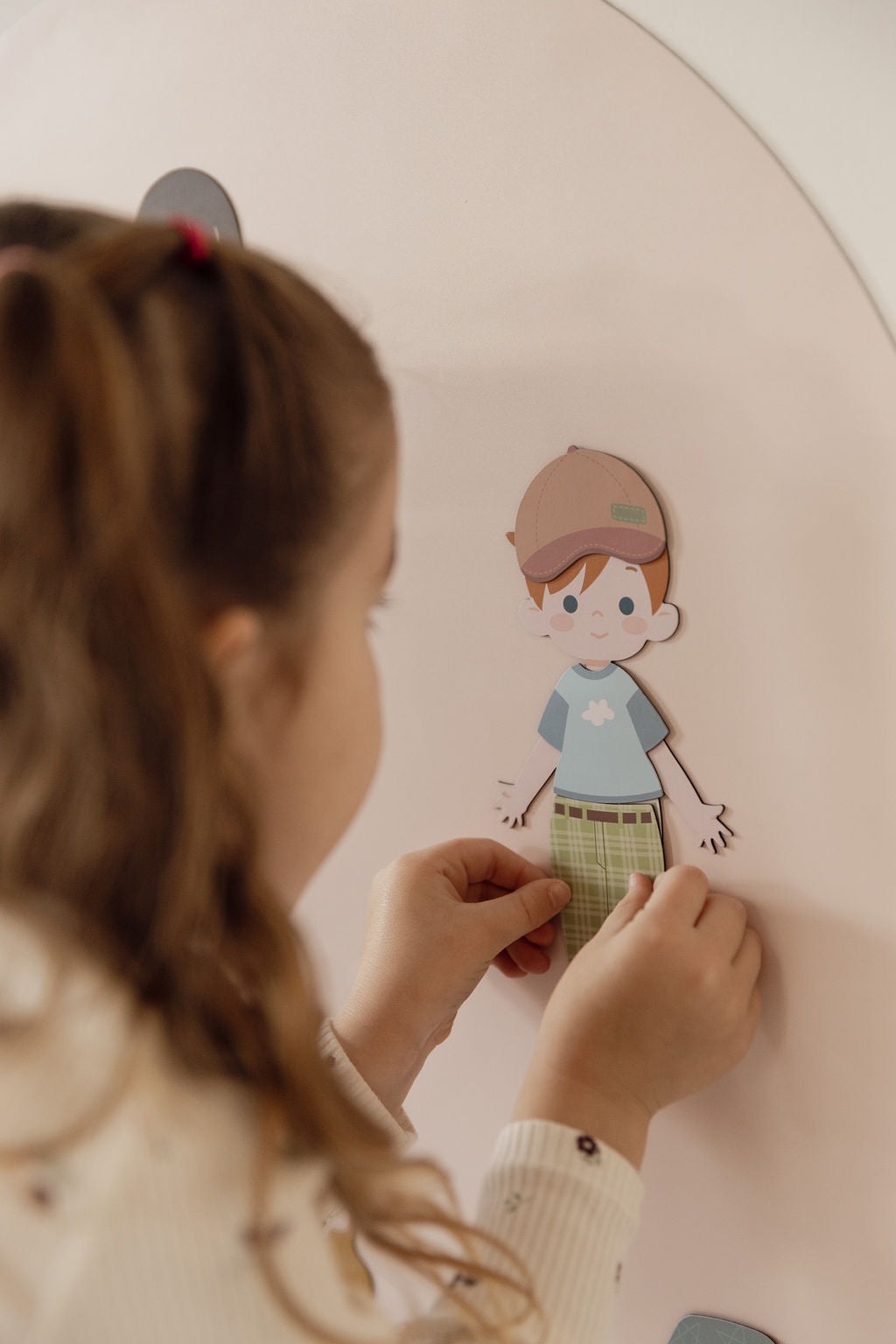 A child's hands placing a magnetic dress-up character in a brown cap, blue shirt and green plaid shorts onto the Wonder Arch.