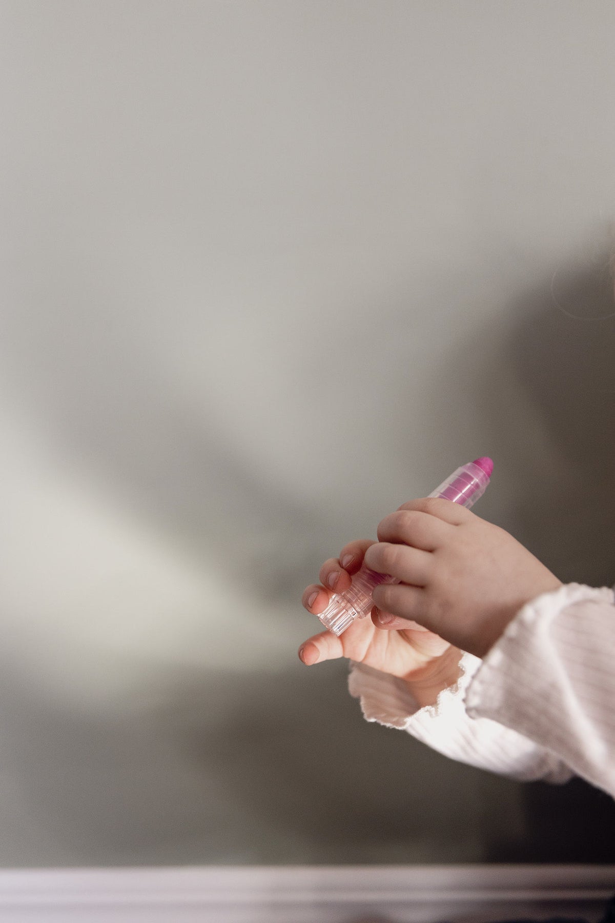 Child's hands holding a pink dust-free chalk stick in front of the Lily Sage Wonder Arch