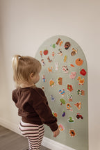 Toddler in a brown jumper playing with farm magnets on the Lily Sage Wonder Arch