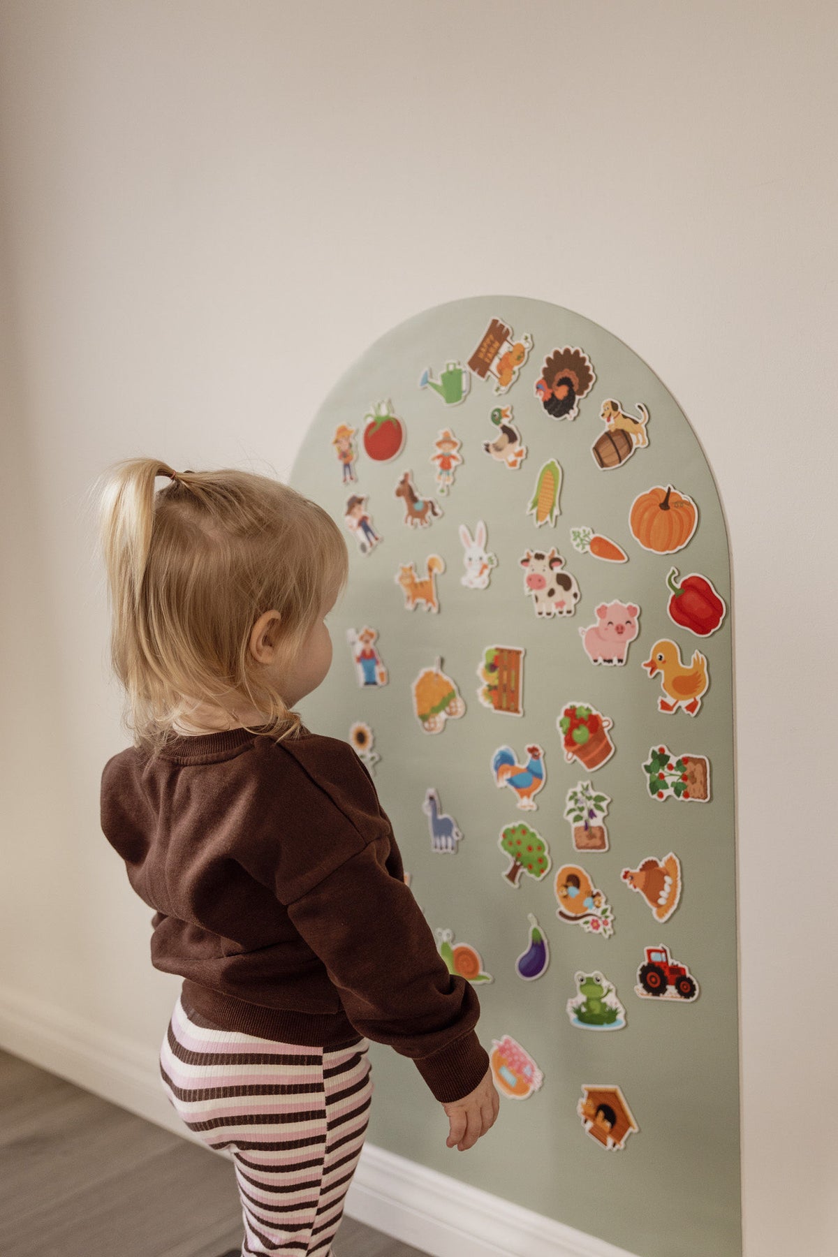 Toddler in a brown jumper playing with farm magnets on the Lily Sage Wonder Arch