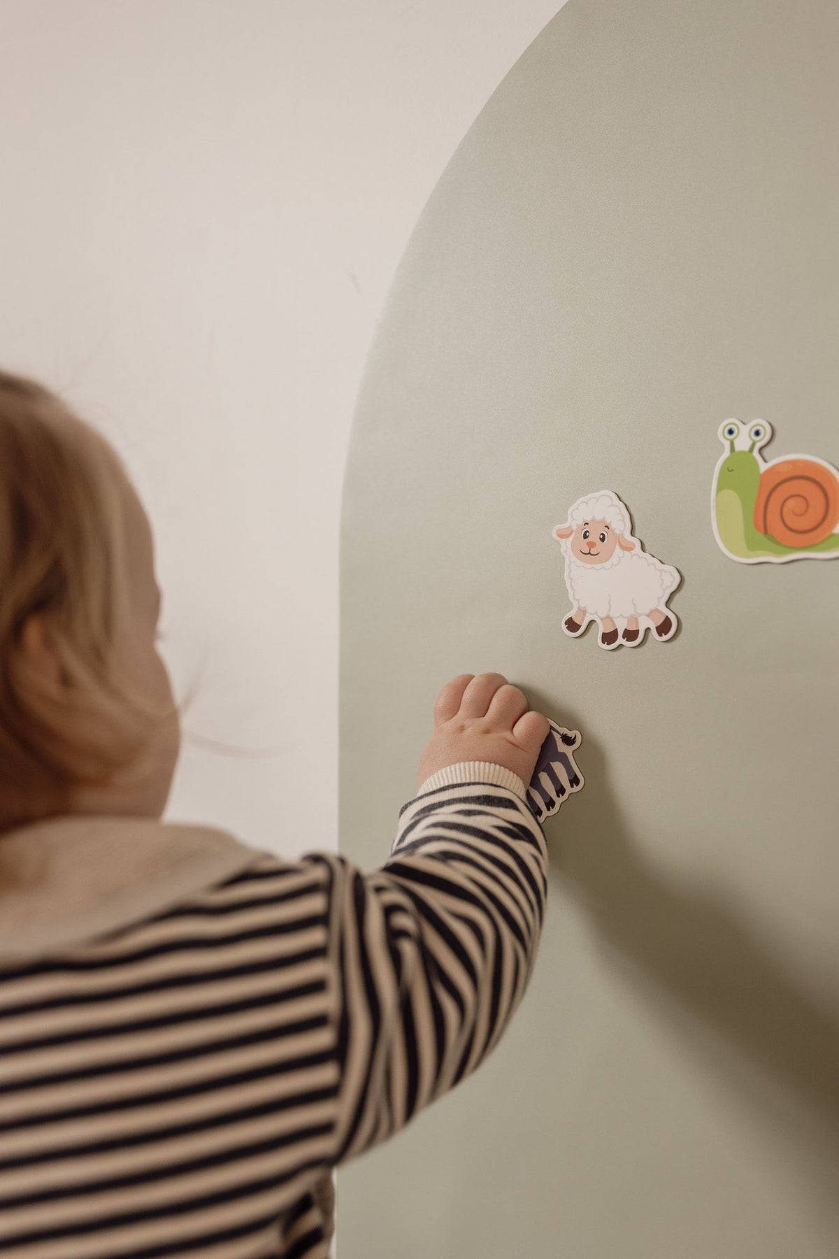 Toddler placing a sheep magnet next to a snail on the Lily Sage Wonder Arch